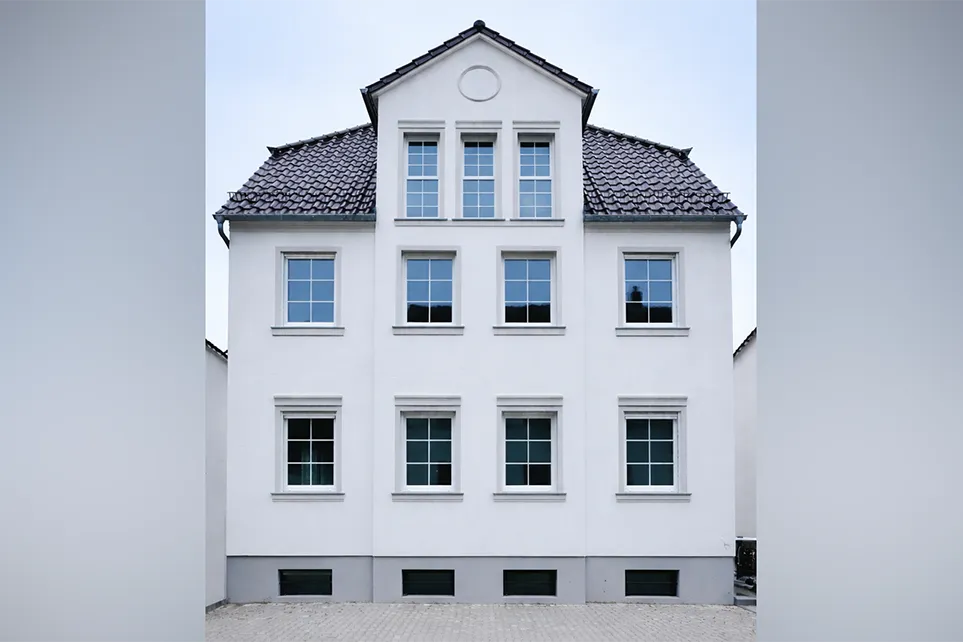 Ein modernes, neu gebautes Einfamilienhaus im Herrenhausstil mit weißer Fassade und vielen Fenstern.