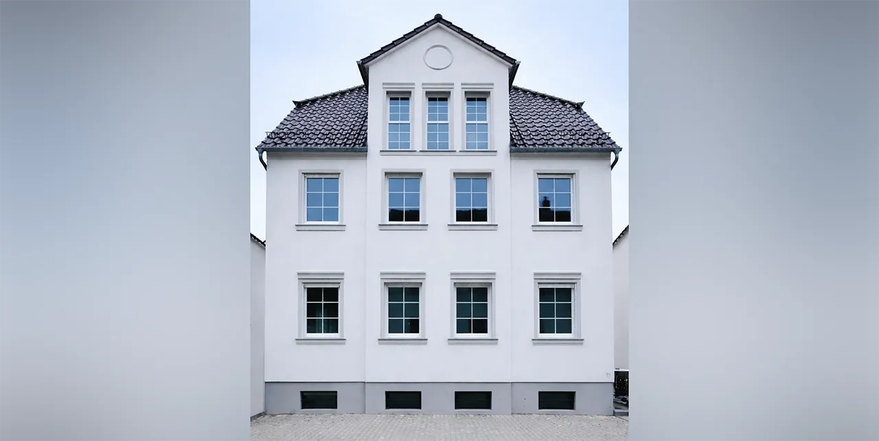 Ein modernes, neu gebautes Einfamilienhaus im Herrenhausstil mit weißer Fassade und vielen Fenstern.