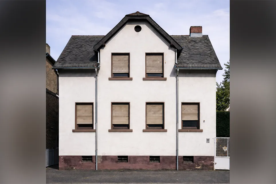 Ein renovierungsbedürftiges Haus mit heller Fassade und heruntergelassenen Rollläden.
