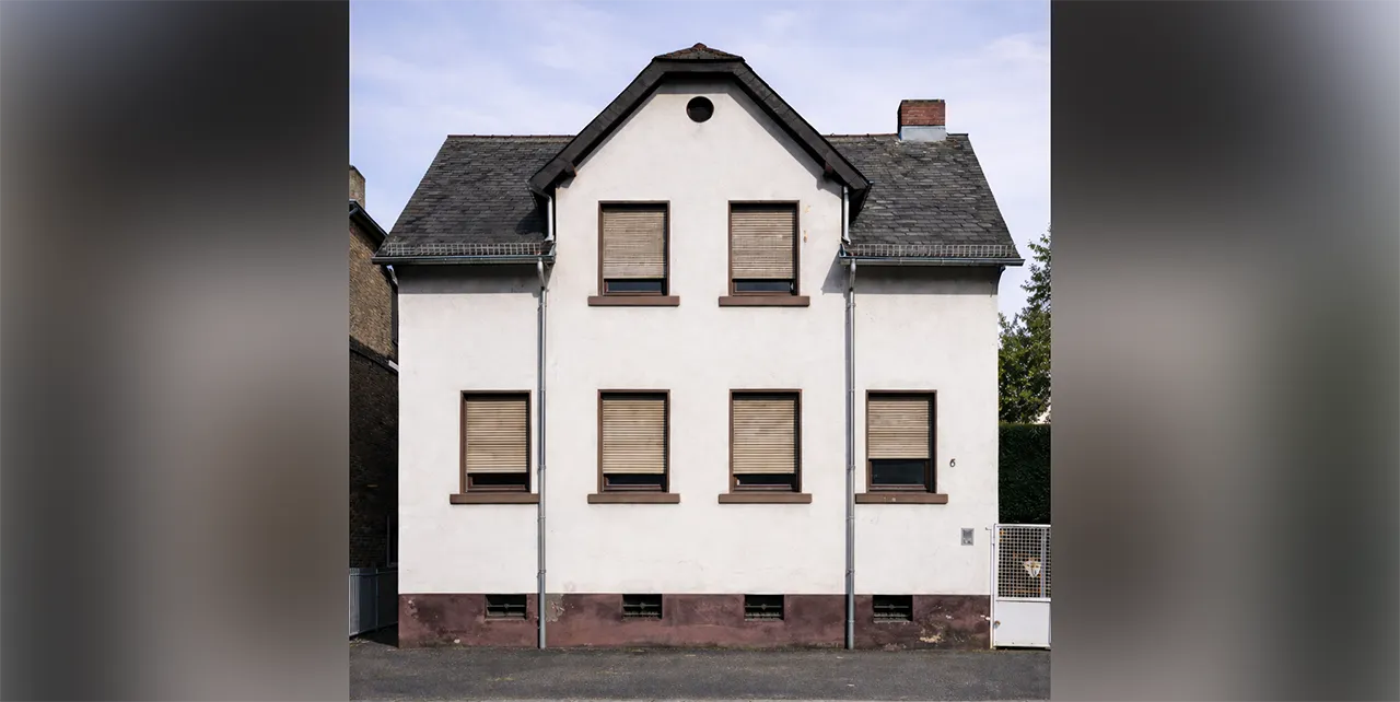 Ein renovierungsbedürftiges Haus mit heller Fassade und heruntergelassenen Rollläden.